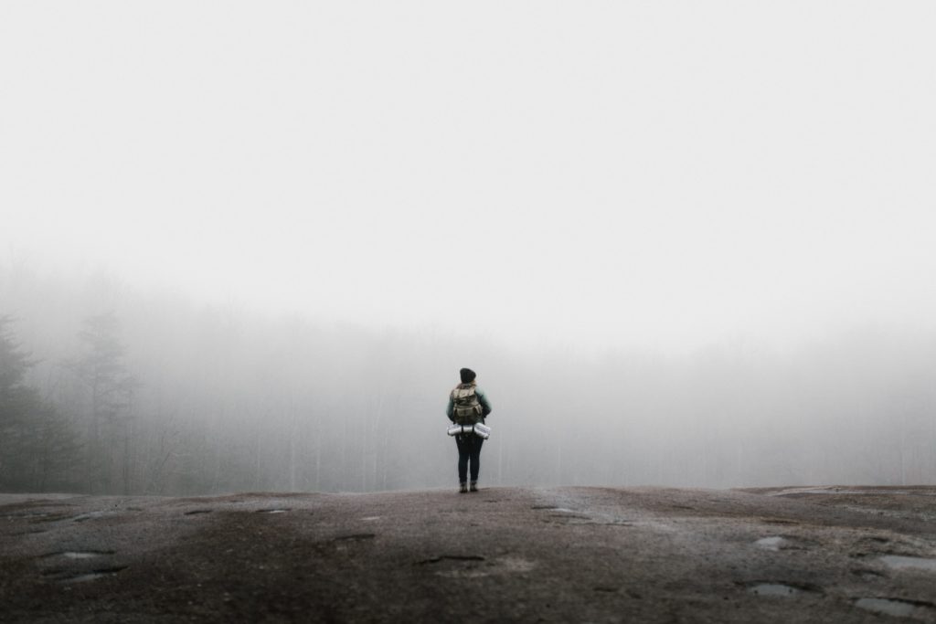 person standing on a cliff in front of a foggy landscape
