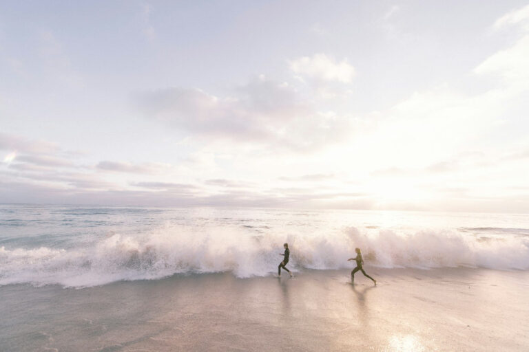 two people playing with the waves on a beach